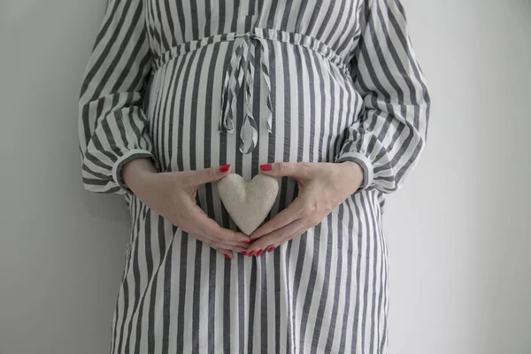 A pregnant woman holding a heart shape in front of here baby bump — Stock Photo, Image