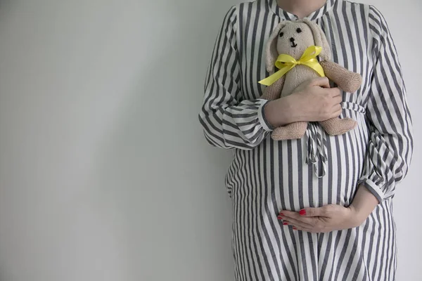 Una mujer embarazada sosteniendo su barriga y un oso de peluche conejito —  Fotos de Stock