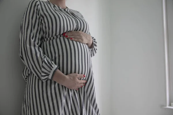 A pregnant woman holding her baby bump stood against a plain background — Stock Photo, Image