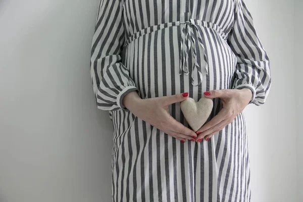 Kobieta w ciąży trzyma kształt serca przed tutaj baby bump — Zdjęcie stockowe