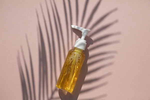 Huile cosmétique naturelle dans une bouteille transparente avec feuille tropicale et ombre — Photo