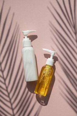 Tropikal palmiye yaprağı gölgesi ile pembe bir arka plan üzerinde şişekozmetik ürünler