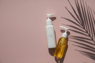 Tropikal palmiye yaprağı gölgesi ile pembe bir arka plan üzerinde şişekozmetik ürünler