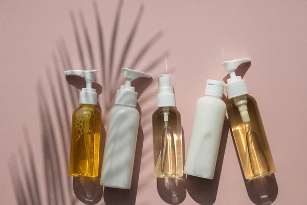 Produits cosmétiques en bouteilles sur fond rose à l'ombre tropicale de palmier — Photo