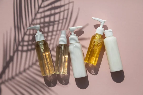 Produits cosmétiques en bouteilles sur fond rose à l'ombre tropicale de palmier — Photo