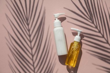 Tropikal palmiye yaprağı gölgesi ile pembe bir arka plan üzerinde şişekozmetik ürünler