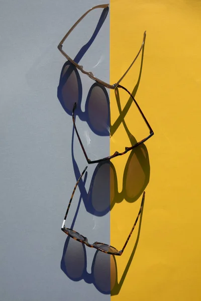 Μεγάλα καλοκαιρινά γυαλιά ηλίου με μακρά σκιά σε κίτρινο και μπλε φόντο — Φωτογραφία Αρχείου