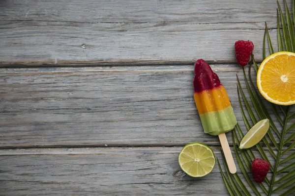 Summer ice lollies with fruit and a tropical palm leaf on a wooden background