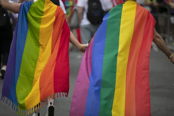 Two gay men wrapped in gay pride flags holding hands with each other