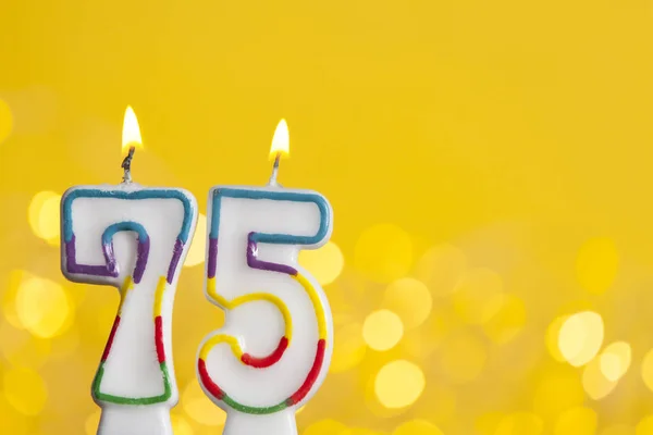 Number 75 birthday celebration candle against a bright lights an — Stock Photo, Image