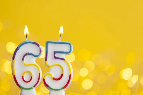 Number 65 birthday celebration candle against a bright lights an — Stock Photo, Image