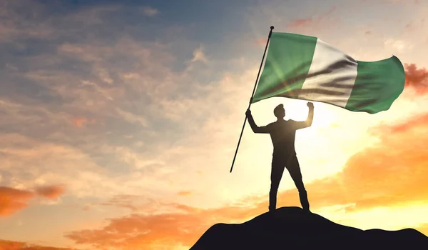 Bandera de Nigeria ondeada por un hombre que celebra el éxito en la cima — Foto de Stock