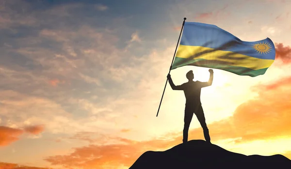 Bandeira de Ruanda sendo acenada por um homem celebrando o sucesso no topo — Fotografia de Stock