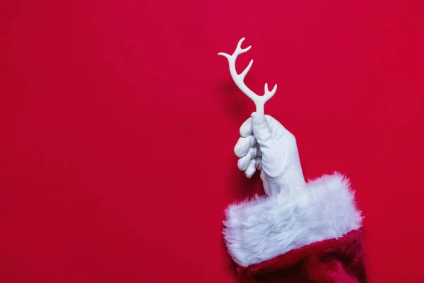 Santa Claus mano de Navidad sosteniendo una cornamenta blanca contra un rojo —  Fotos de Stock