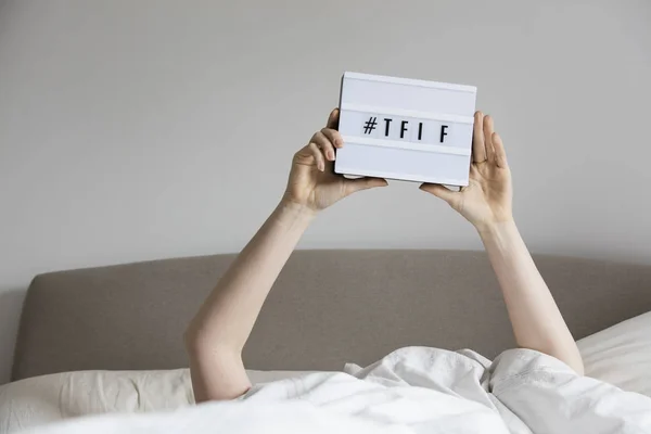 Mujer en la cama debajo de las sábanas sosteniendo un signo TFIF — Foto de Stock