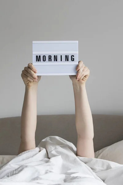 Γυναίκα στο κρεβάτι κάτω από τα σεντόνια κρατώντας ένα πρωινό σημάδι — Φωτογραφία Αρχείου