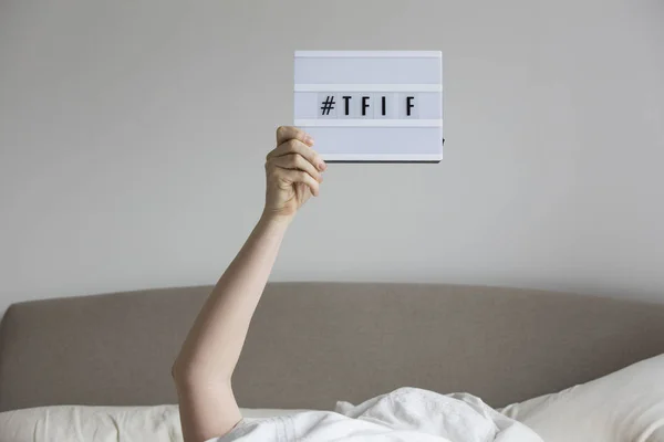 Female in bed under the sheets holding up a TFIF sign — Stock Photo, Image