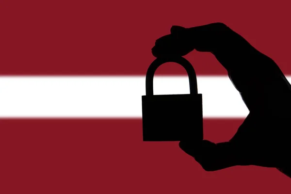 Ασφάλεια της Λετονίας. Σιλουέτα χεριού που κρατά ένα λουκέτο πάνω από το — Φωτογραφία Αρχείου