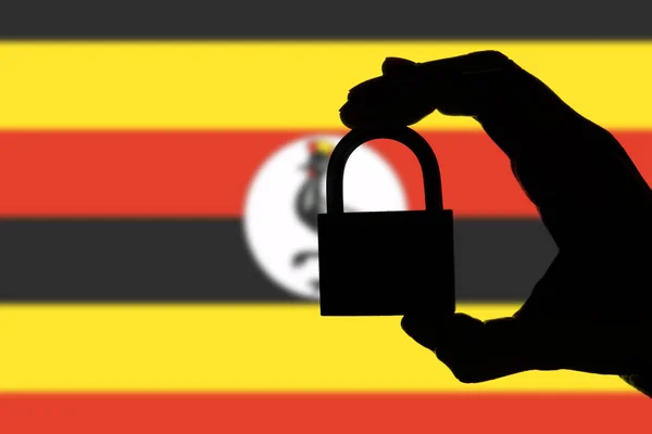 Uganda security. Silhouette of hand holding a padlock over natio — Stock Photo, Image