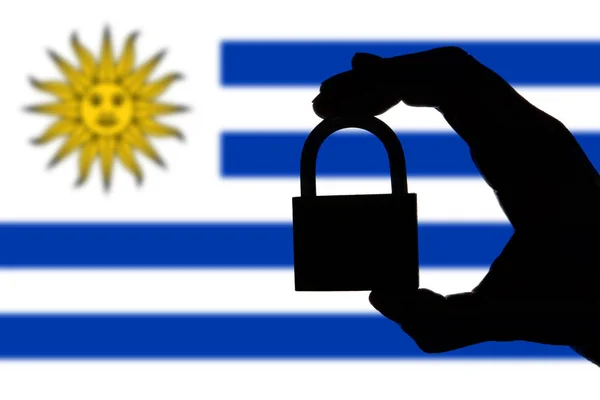 Uruguay security. Silhouette of hand holding a padlock over nati