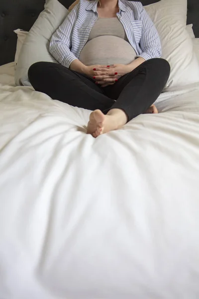 Una joven embarazada descansando en casa sentada en una cama. Madre embarazada. — Foto de Stock