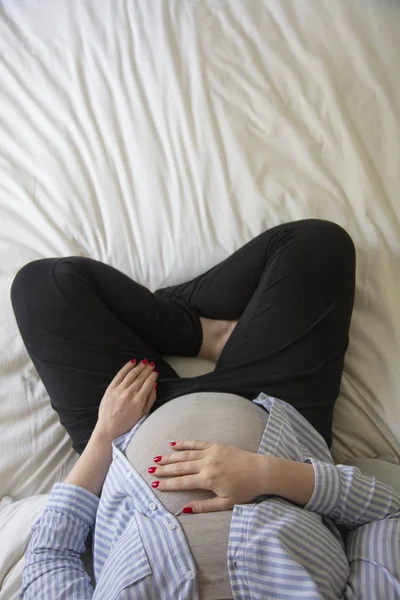 Mladá těhotná žena, která odpočívá doma a sedí na posteli. Matka s očekáváním — Stock fotografie