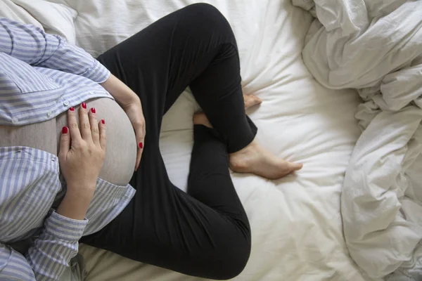 Una joven embarazada descansando en casa sentada en una cama. Madre embarazada. — Foto de Stock