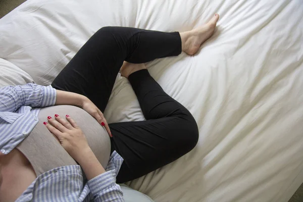 Una giovane donna incinta che riposa a casa seduta su un letto. Madre in attesa — Foto Stock