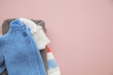 Pastel pembe arka plan üzerinde sevimli örme bebek kıyafetleri düzeni