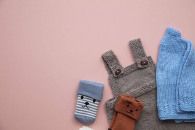 Pastel pembe arka plan üzerinde sevimli el yapımı örme bebek kıyafetleri düzeni