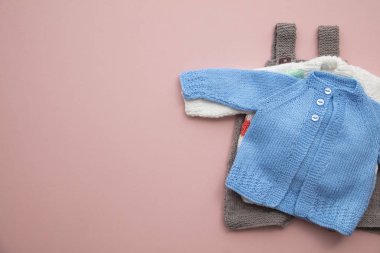 Pastel pembe arka plan üzerinde sevimli örme bebek kıyafetleri düzeni