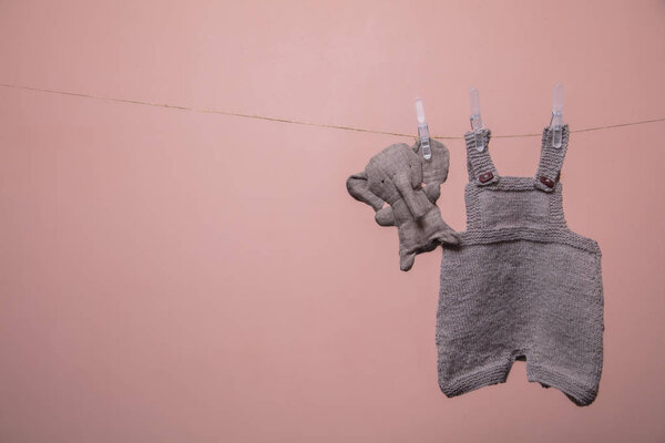 Handmade knitted baby clothes hanging on a line with a toy