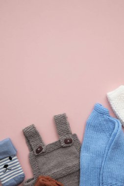 Pastel pembe arka plan üzerinde sevimli el yapımı örme bebek kıyafetleri düzeni