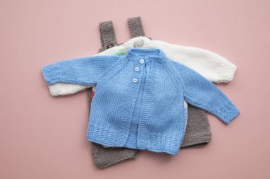 Pastel pembe arka plan üzerinde sevimli örme bebek kıyafetleri düzeni