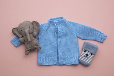 Pastel pembe arka plan üzerinde sevimli el yapımı örme bebek kıyafetleri düzeni
