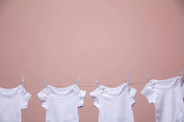 White baby body suit hanging from a line against a pink background