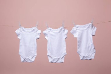 Beyaz bebek vücut elbisesi pembe bir arka plan karşı bir çizgi asılı