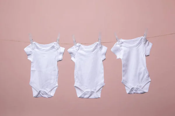 Traje de bebé blanco colgando de una línea sobre un fondo rosa —  Fotos de Stock