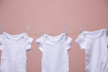 Beyaz bebek vücut elbisesi pembe bir arka plan karşı bir çizgi asılı