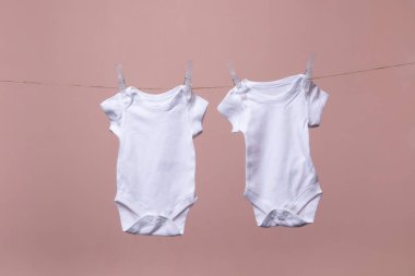 Beyaz bebek vücut elbisesi pembe bir arka plan karşı bir çizgi asılı
