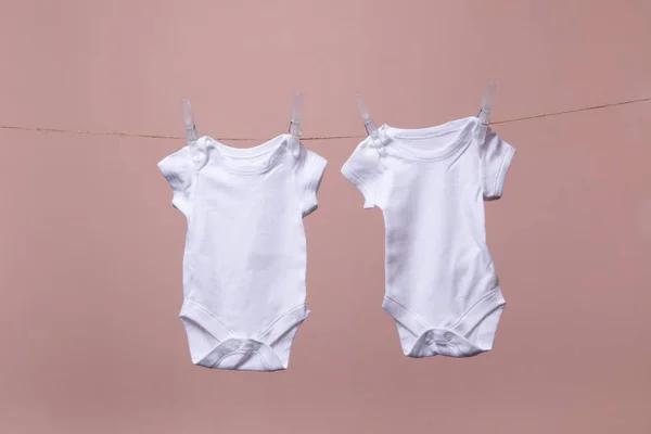 White baby body suit hanging from a line against a pink background — Stock Photo, Image