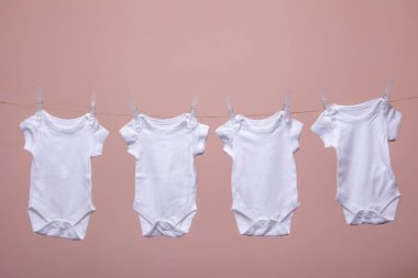 Beyaz bebek vücut elbisesi pembe bir arka plan karşı bir çizgi asılı