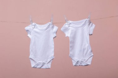 Beyaz bebek vücut elbisesi pembe bir arka plan karşı bir çizgi asılı