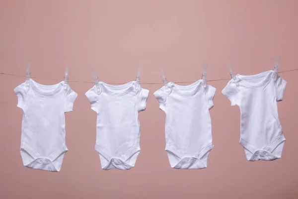 Traje de bebé blanco colgando de una línea sobre un fondo rosa —  Fotos de Stock