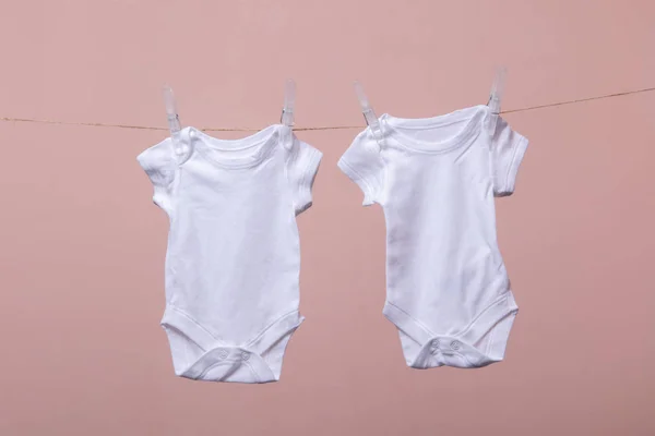 Traje de bebé blanco colgando de una línea sobre un fondo rosa —  Fotos de Stock