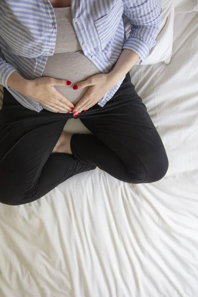 Una joven embarazada descansando en casa sentada en una cama. Madre embarazada. — Foto de Stock