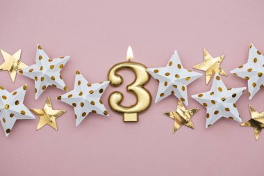 3 numara altın mum ve pastel pembe arka plan üzerinde yıldız
