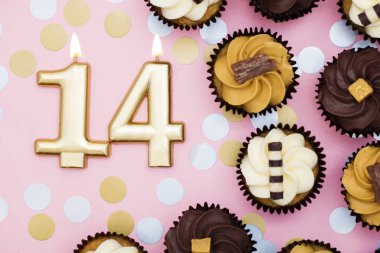 Bir pastel pembe backgr karşı cupcakes ile Sayı 14 altın mum