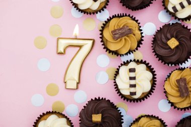 Bir pastel pembe backgro karşı cupcakes ile Sayı 7 altın mum