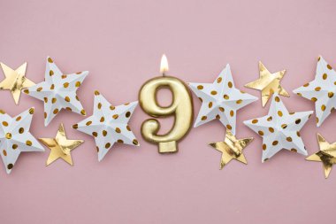9 numara altın mum ve pastel pembe arka plan üzerinde yıldız